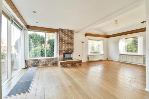 A spacious living room with large windows allowing for natural light, featuring wooden floors and a