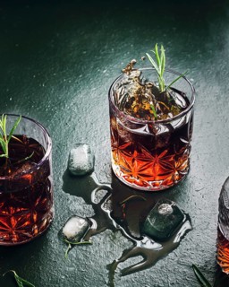 A dramatic scene of whiskey splashing in a glass garnished with rosemary, surrounded by scattered