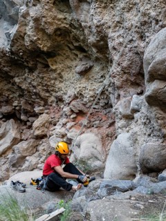 A climber prepares for a traditional climb on a rocky natural cliff. Wearing safety gear, they