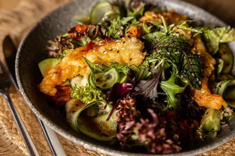 A vibrant bowl of green salad topped with crispy, batter-fried king prawns, garnished with sesame