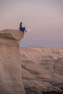 Unrecognizable woman in a flowing blue dress perched on a white rock formation at Sarakiniko,