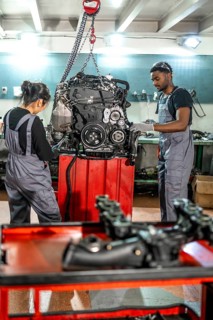 Two auto mechanics inspecting a car engine hanging from a chain hoist in a professional workshop
