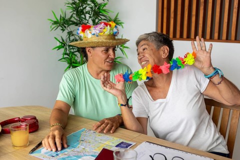 Two older women adorned with a flower lei and a straw hat smiling cheerfully while planning their