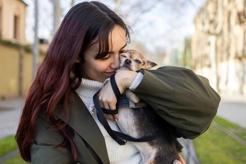 A woman warmly cuddles her small chihuahua outdoors, showcasing a tender moment of affection. The