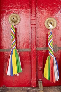 Vibrant red doors adorned with colorful braided fabric hangings, set against the backdrop of