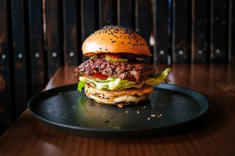 A close-up of a delicious hamburger served on a dark plate. The burger is topped with fresh