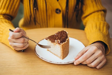 A person in a cozy yellow sweater enjoys a slice of chocolate-topped cake, poised with a fork The