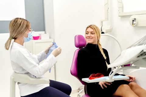 A female dentist wearing a mask prepares for a procedure in a modern dental clinic, while a young