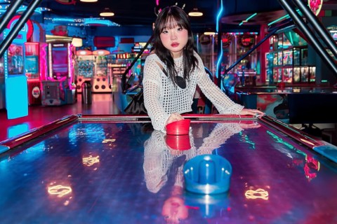 An Asian Gen Z girl having fun in an arcade, surrounded by vibrant neon lights and colorful games
