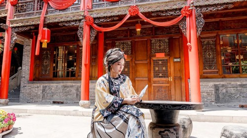 A woman in Qing Dynasty attire sits outside a traditional building in Pingyao, China, intently