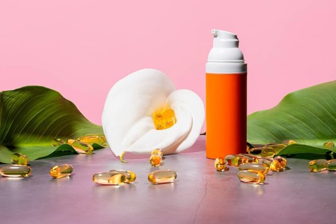 An elegant cosmetic setup featuring an orange pump bottle, surrounded by yellow omega-3 supplement
