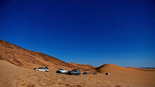Night shot of a desert camp with tents and cars under a starry sky, adventure camping with off-road