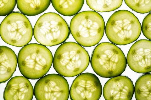 A close up image of green cucumber slices arranged in a seamless pattern. The fresh and vibrant