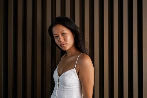 A Chinese woman in a summer outfit stands against a city backdrop, exuding confidence. The warm