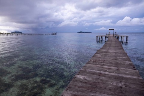 A serene view from a wooden pier on Waigeo Island, Indonesia. Cloudy skies enhance the tranquil