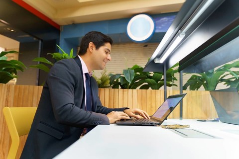 Young Chilean businessman working on a laptop in a modern office setting, surrounded by green