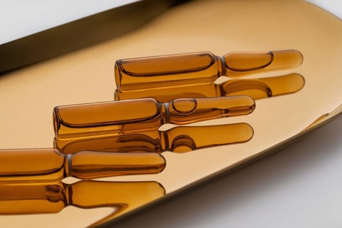 Transparent glass ampoules filled with golden anti-aging serum, elegantly displayed on a reflective