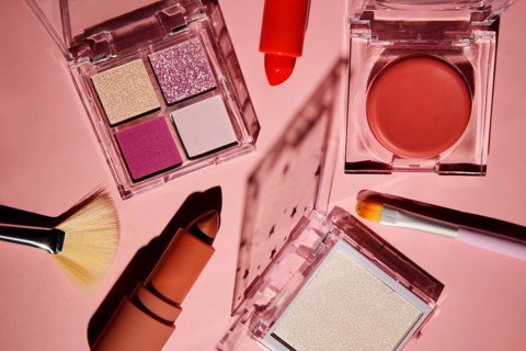 Top view of a vibrant makeup set on a pink background, featuring eyeshadow palettes, a lipstick,