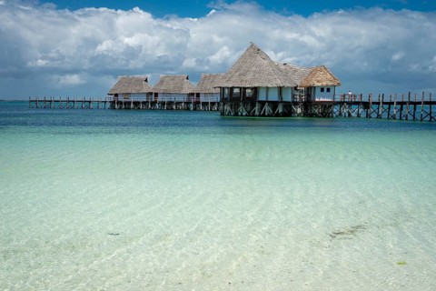 A beautiful row of traditional thatched-roof overwater bungalows connected by a wooden pier,