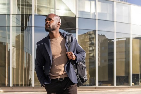 A professional cuban man in a blazer walks with confidence in a cityscape. The glass building