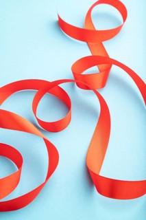 Red coral ribbon on a blue pastel background. Celebration concept. Side view, copy space