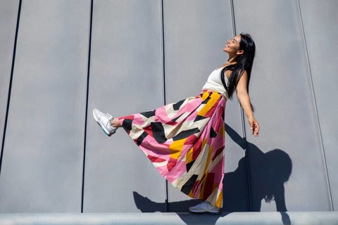 A woman in a vibrant, colorful outfit stands against modern architectural panels. Her attire