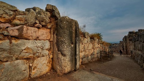 Cyclopean wall, gate, old paved path between high stone walls under a cloudy sky, Tiryns, ancient