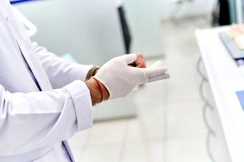 Dentist carefully putting on sterile gloves in a modern dental clinic. White lab coat and