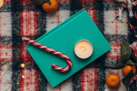 Top view of a festive holiday display featuring a lit candle, candy cane, book, and fresh