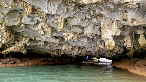 A boat navigates through a natural rock cave with impressive stalactite formations, natural scenery