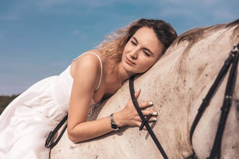 A young woman leans gently on a horse, enjoying a tranquil moment in a sunny field. Wearing a white