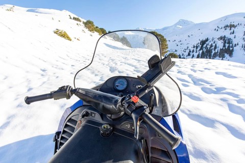 View from the seat of a snowmobile on a sunny winter day, surrounded by pristine snowy mountains