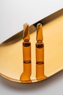 Three brown glass ampoules filled with anti-aging serum, elegantly presented on a reflective golden
