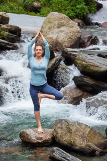 Woman in Hatha yoga balance yoga asana Vrikshasana tree pose at waterfall outdoors