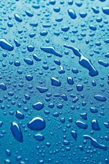 Close up image of water droplets on a smooth blue surface. The droplets vary in size, creating a