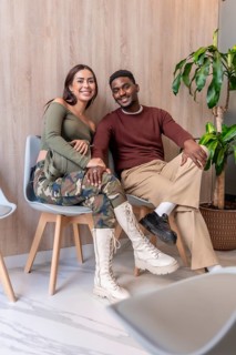 Pregnant woman and her partner sitting and smiling in contemporary dental clinic waiting area,