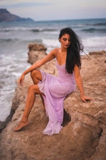 Posing of a young brunette Caucasian in a pink dress, on the beach having fun by the sea