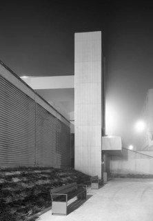 An urban elevator emerges amidst mist and fog, illuminated subtly at night. The modern design
