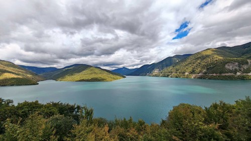Calm lake surrounded by wooded mountains under partly cloudy sky, Georgia