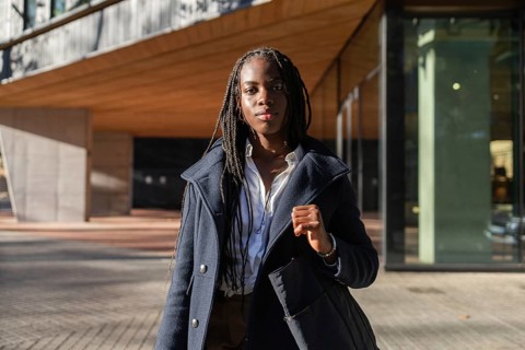 An African American businesswoman with braided hair enjoys a break outdoors, dressed smartly in a