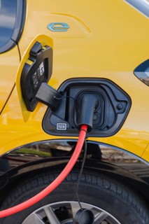 Close-up of an electric car charging with a vivid red cable at a station. The yellow vehicle's