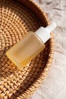 A minimalist glass dropper bottle rests on a woven basket under gentle sunlight. The scene exudes