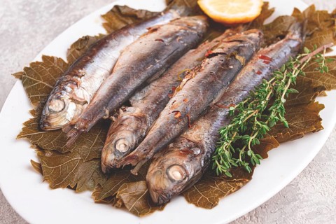 Baked fish, in grape leaves, with spices, on a white plate, homemade
