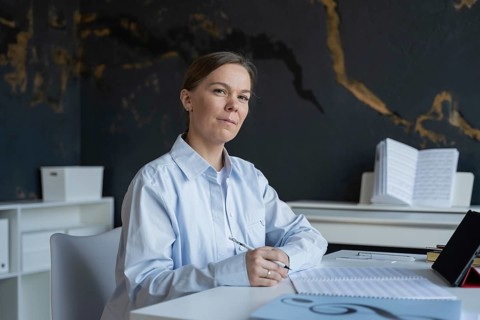 A focused woman sitting at a table writes notes for an upcoming piano lesson. She is surrounded by