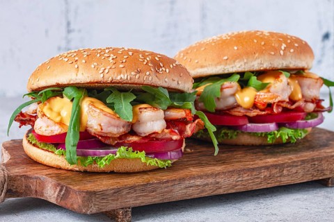 Two shrimp burgers and buns with sesame seeds, bacon, lettuce, tomatoes and onions, On a wooden