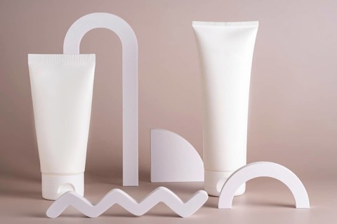 Elegant display of white skincare tubes surrounded by minimalist geometric shapes on a beige