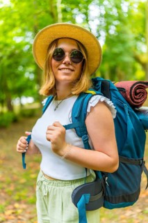 Vertical portrait of a young woman wearing a backpack smiling while walking through a forest path