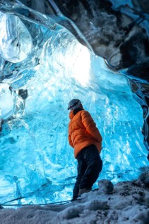 A man in an orange jacket with his back turned in a glacier cave in Iceland in winter