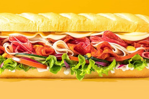 Close-up of a stacked deli sandwich, styled on a vibrant monochrome backdrop, with frontal lighting