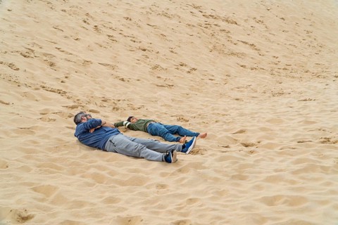 A father and son lie on the dune of Pilat, enjoying a moment of relaxation in France. The serene